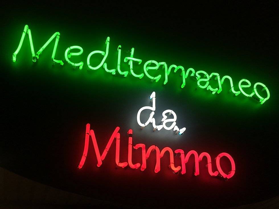 Ein italienisches Restaurant deren Leuchtschrift aus einer Neon-Handschrift in verschiedenen Farben leuchtet wirkt im Dunkeln schlicht und ansprechend. Die Neon-Schreibschrift ist handgefertigt und mundgeblasen.