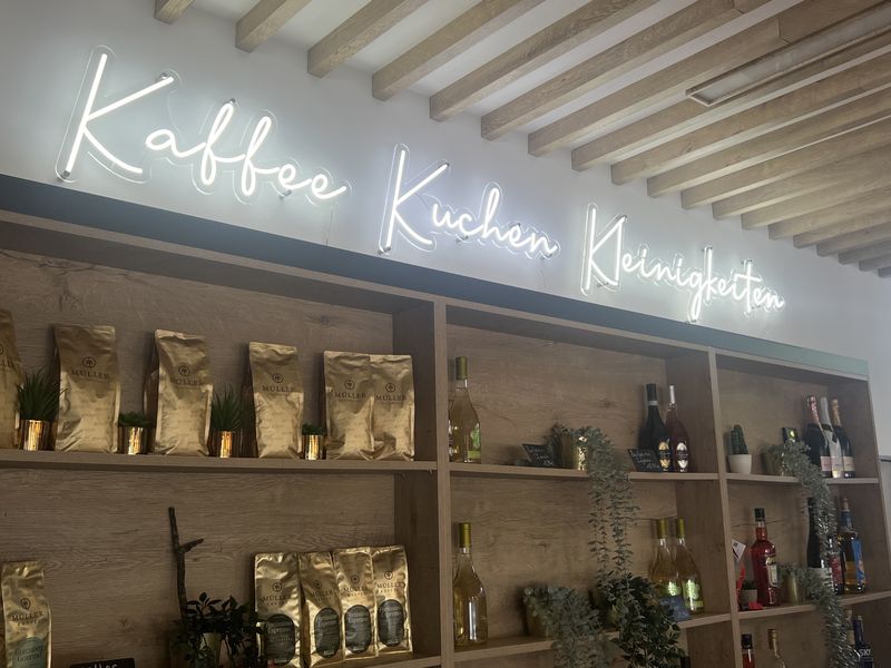 Innenwerbung mit LED-Neon zum Blickfang im Kaffee. Die weiß leuchtender Leucht-Handschrift ist eine Lichtwerbung, wo das Angebot „Kaffee, Kuchen, Kleinigkeiten“ zu sehen ist.  Es schafft eine einladende, warme Atmosphäre im Gastraum. 