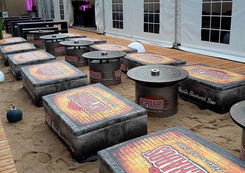 Desperados-Vintage Look-Lounge Lounge Möbel mit Strandfeeling mit Desperados-Öl-Fass-Tische und gepolstereten Sitzkisten laden Gäste zum verweilen ein. Die Kombination aus rustikalem Industrie-Vintage Look des Fasses und warmem Holz schafft einen modernen, urbanen Stil mit sommerlichem Flair. Die Verbindung aus Lounge-Möbeln natürlichen Dekorationselementen und dem individuell gestalteten Fass-Stehtisch, unterstützt gezielt die Aufenthaltsqualität.