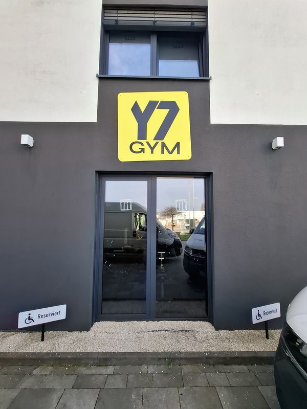 Außenwerbung am Haupteingang des Y7 GYM. Das markante gelbe Alu-Dibond-Schild mit schwarzem 