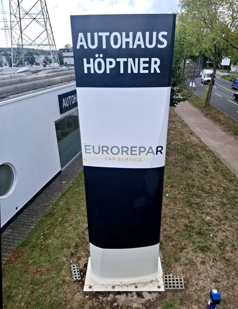 Teilweise neu folienkaschierter Werbepylon des Autohauses Höptner mit EUROREPAR-Beschriftung während der Montage.