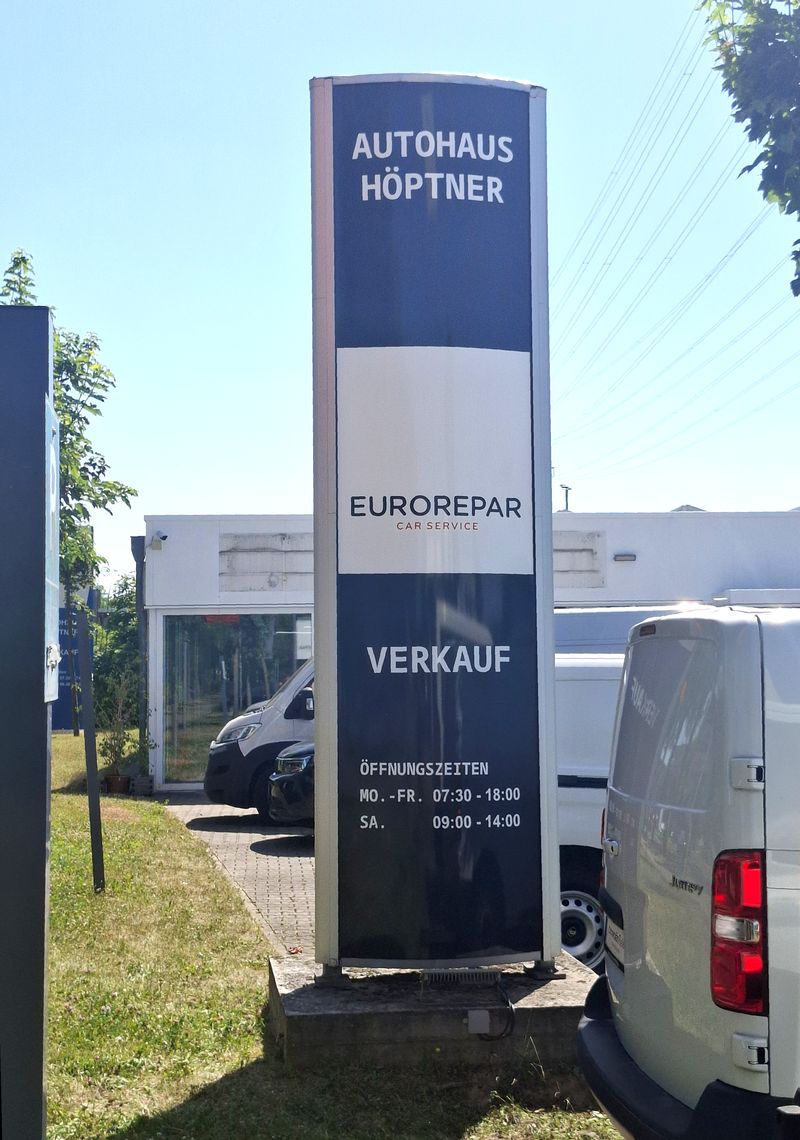 Pylon-Neubeschriftung Autohaus Höptner-Folienkaschierung Für das Autohaus Höptner wurde ein bestehender, rund 4 Meter hoher Werbepylon durch eine umfassende Folienkaschierung optisch neu gestaltet. Ziel war es, die vorhandene Werbeanlage an das aktuelle Erscheinungsbild des Autohauses und der darauf präsentierten Marken anzupassen.