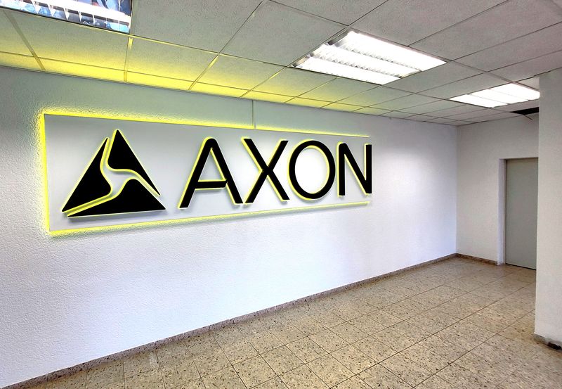 Das Logo AXON mit der LED-Rückbeleuchtung erzeugen einen Lichteffekt, bei dem das Licht an der Haube reflektiert wird und die Buchstaben dadurch als Kontur erscheinen. Dies verleiht den Buchstaben eine dreidimensionale und auffällige Optik, wobei die Haube eine Konturbeleuchtung bis zur Decke ausstrahlt. Die LED-Rückbeleuchtung sorgt zudem für eine energiesparende und langlebige Beleuchtungslösung.