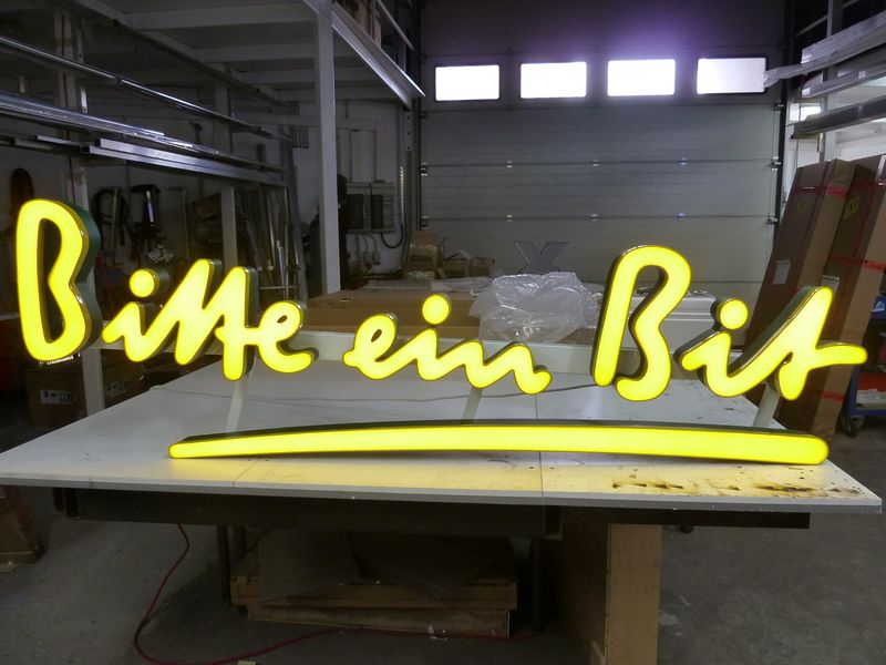Die Leuchthandschrift aus Acryl mit dem Bitburger Logo in unserer Werkstatt. Die markante, geschwungene Handchrift wird durch eine gleichmäßige, intensiv gelbe LED-Ausleuchtung perfekt in Szene gesetzt. Diese Form der professionellen Lichtwerbung sorgt für maximale Aufmerksamkeit und eine starke Markenpräsenz.