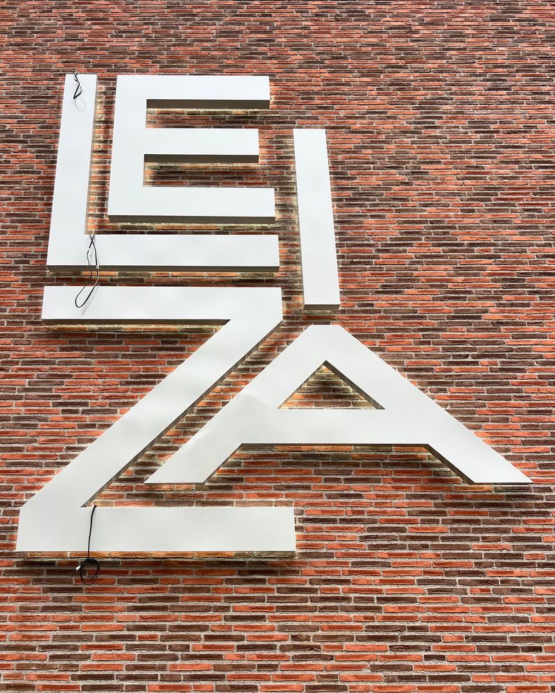 Lichtwerbeanlage Leiza Fertige Montage der dreidimensionalen Profilbuchstaben, die das Firmenlogo Leiza zeigen. Ein gleichmäßiger Lichtschatten auch Halo-Beleuchtung oder Corona genannt, entsteht durch eine Rückbleuchtung mit Abstandshalterung. Eine Lichtwerbeanlage mit gleichmäßige und energieeffiziente Ausleuchtung als Außenwerbung.