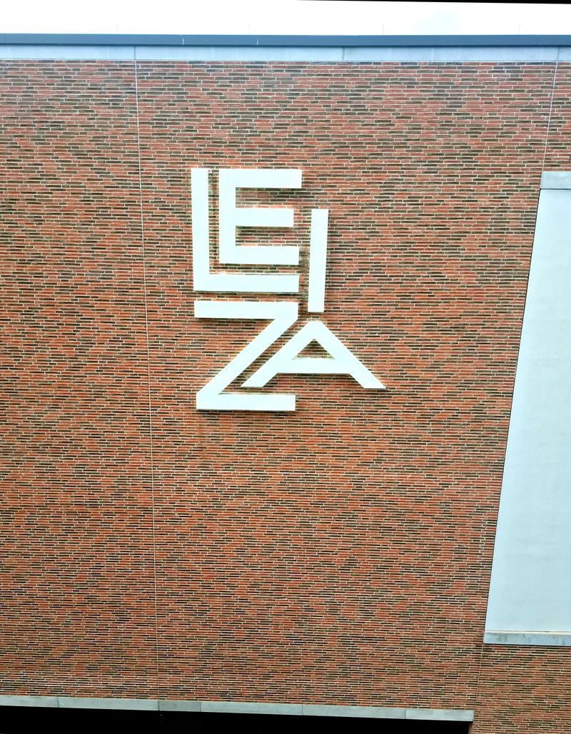Leiza Fassaden-Werbeanlage Weiße Aluminium-Profilbuchstaben des LEIZA-Logos mit indirekter LED-Rückbeleuchtung (Halo-Beleuchtung) hinter den Profilbuchstaben direkt an einer modernen Klinkerfassade montiert. Die hochwertige Fassadenwerbung sorgt tagsüber für eine elegante Optik und nachts für eine gleichmäßige Schattenbeleuchtung.