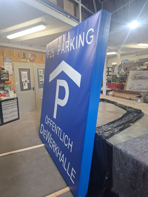 Der fertig aufgebaute Leuchtkasten mit der Beschriftung „F25 Parking – Öffentlich Die Werkhalle“ steht nach der Fertigung in der Werkstatt zur Vorbereitung auf die Montage. Die robuste Konstruktion ist für den Einsatz als gut sichtbare Außenbeschilderung ausgelegt.